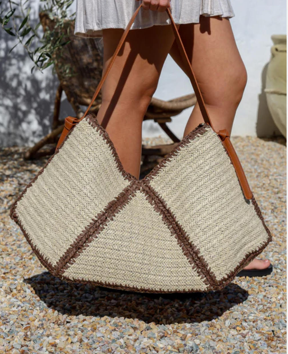 Woven handbag with geometric pattern held by a person outdoors.
