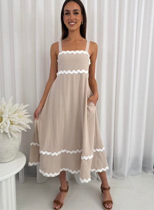 Woman wearing a beige dress with white trim against a white curtain background