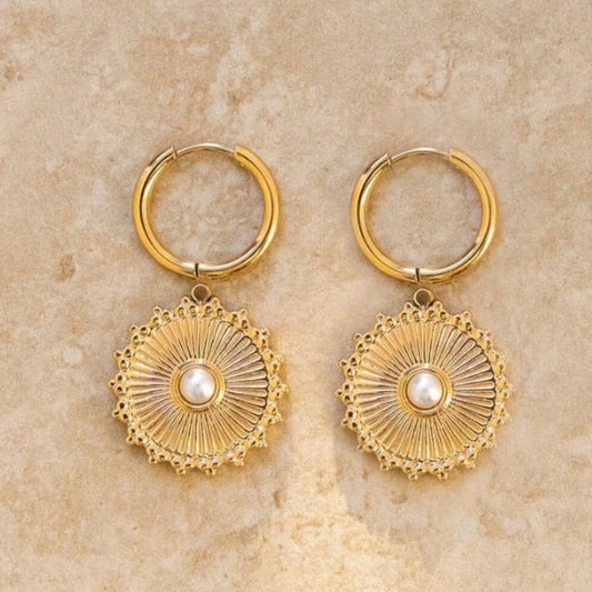 Gold hoop earrings with circular designs and pearl-like centers on a beige stone background