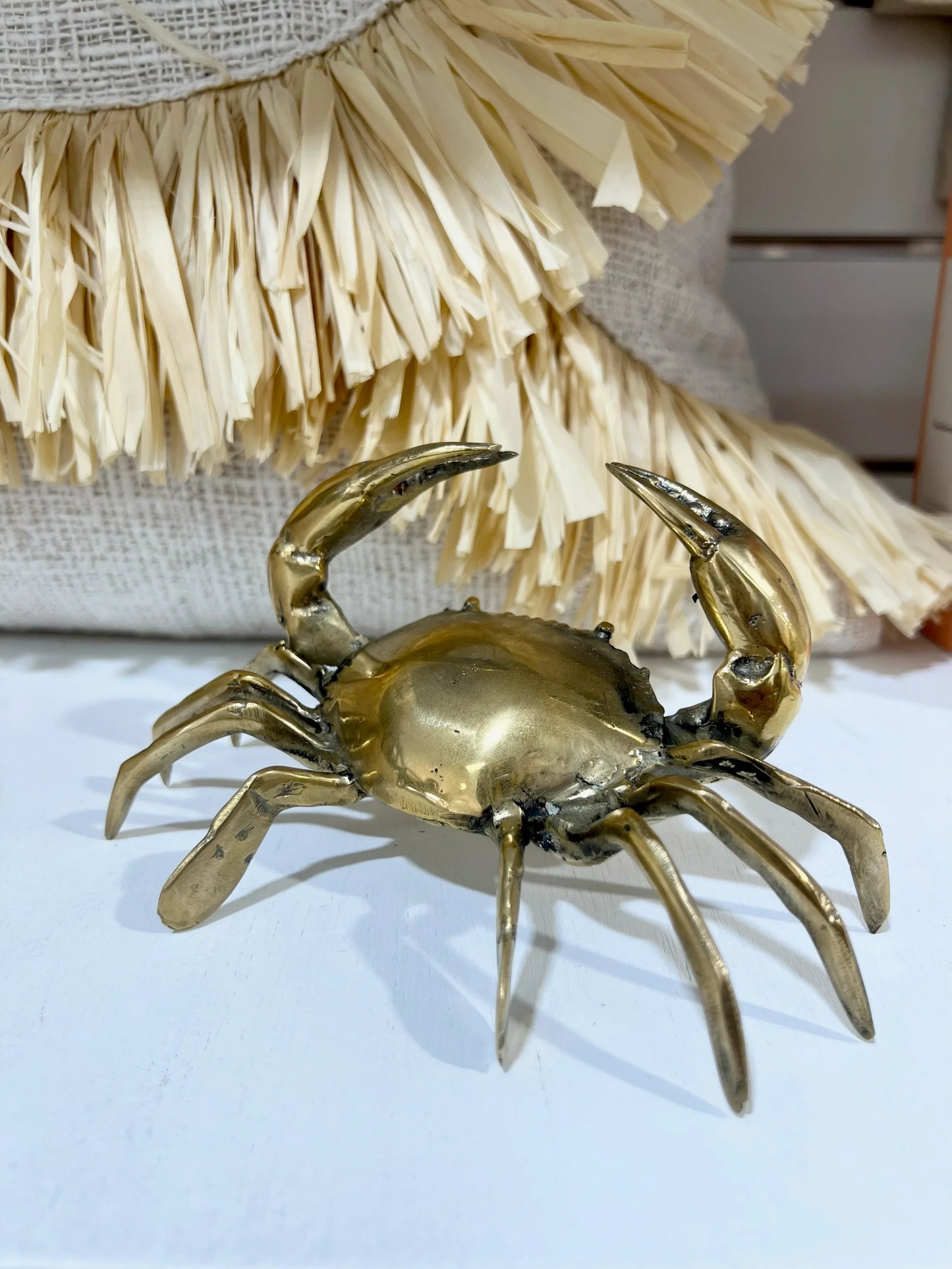 Brass crab figurine on a white surface with a textured beige background