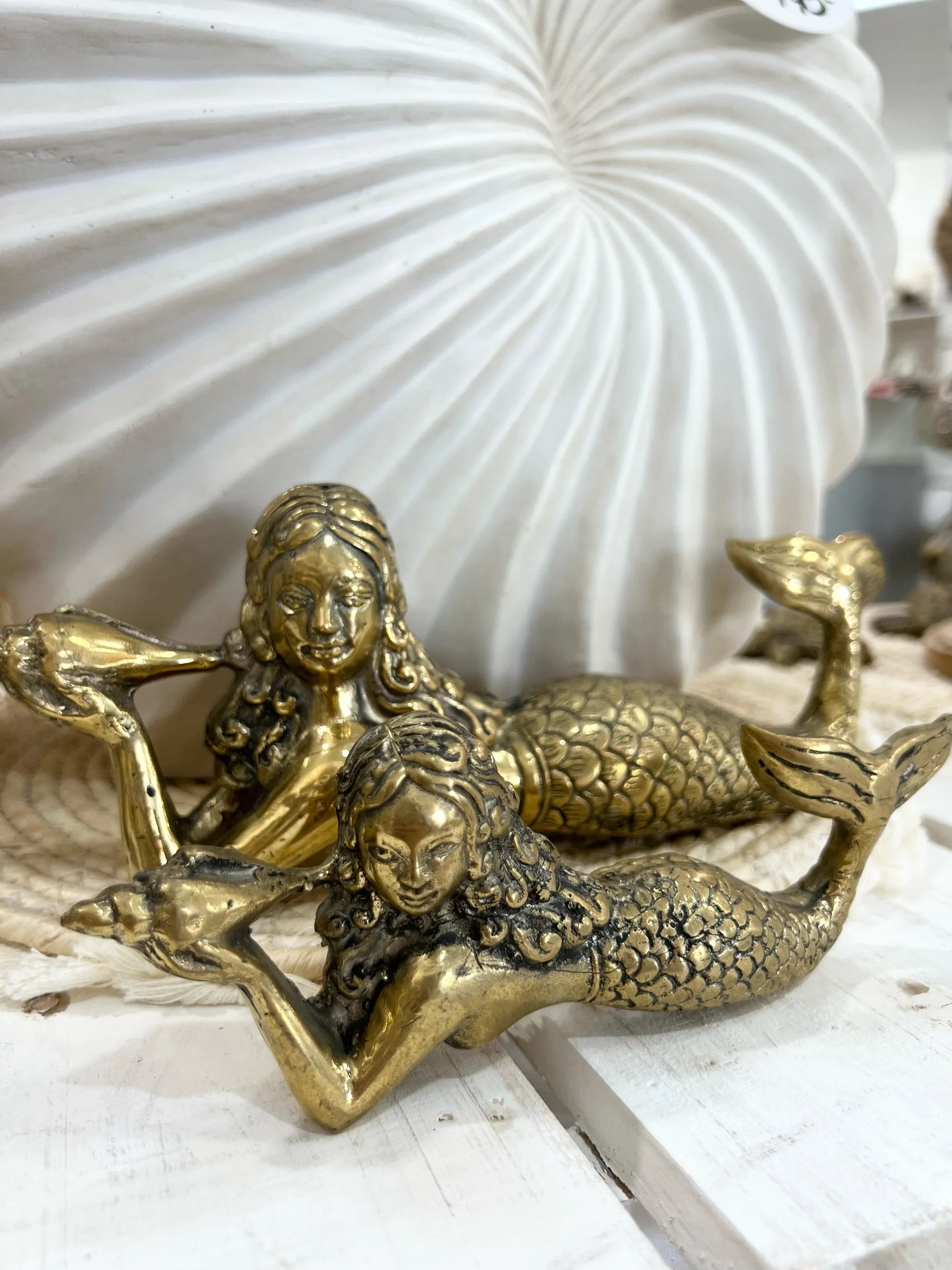 Bronze mermaid figurines on a white surface with a large shell in the background