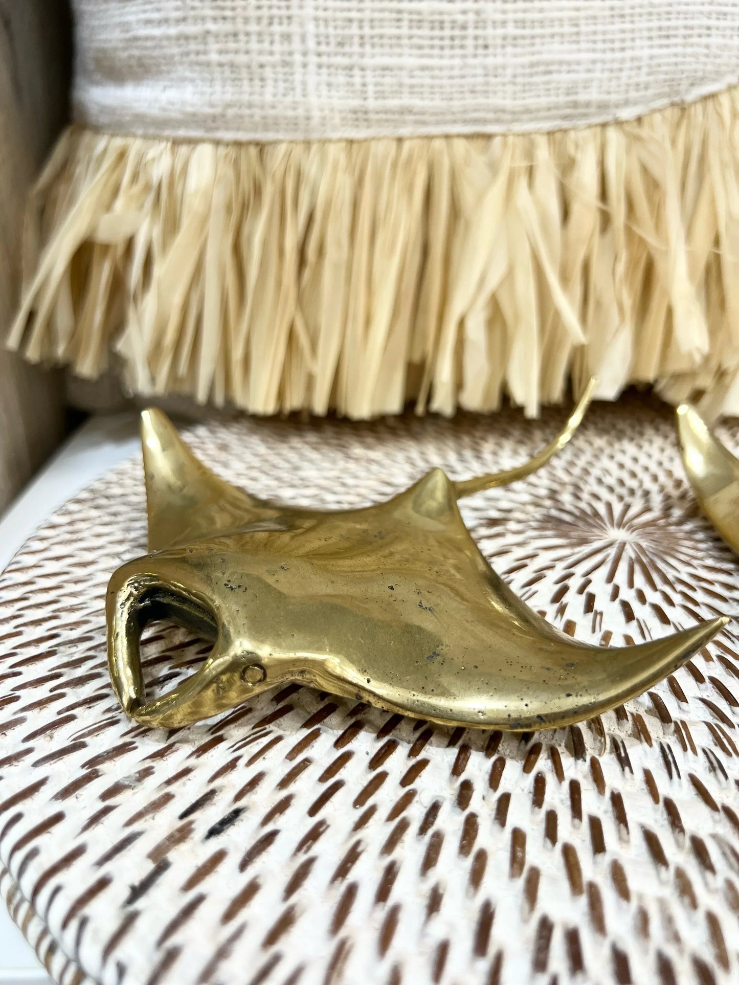 Brass stingray-shaped bottle opener on a textured surface with fringe