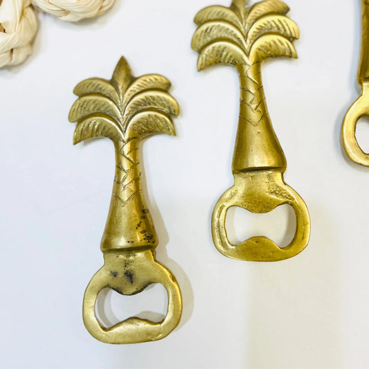 Two brass bottle openers with palm tree design on a white background