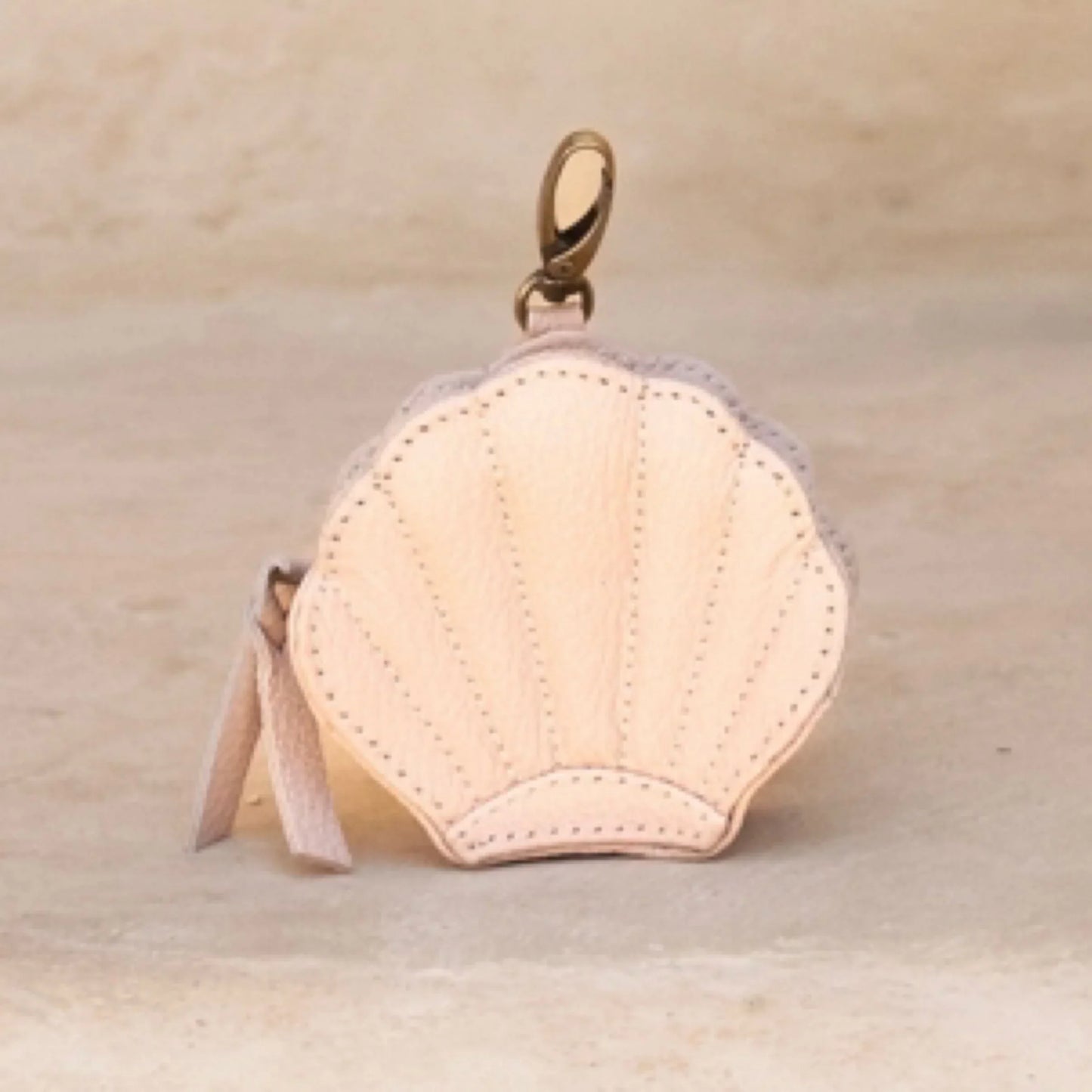 Pink leather keychain purse with a gold clasp on a beige background
