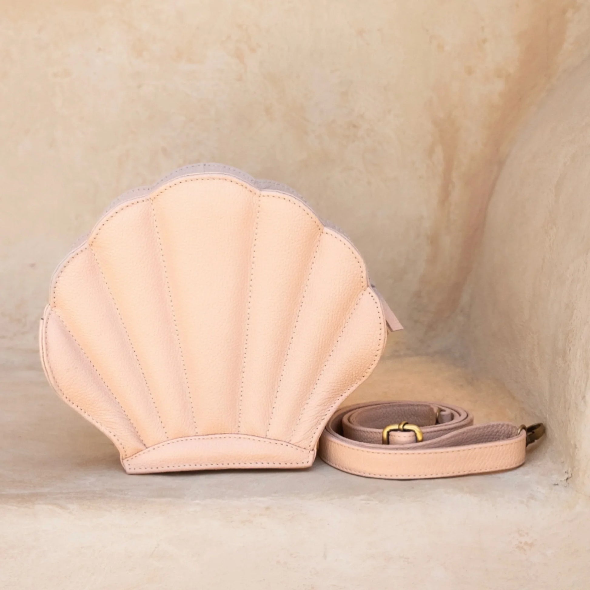 Shell-shaped handbag with a strap on a beige background