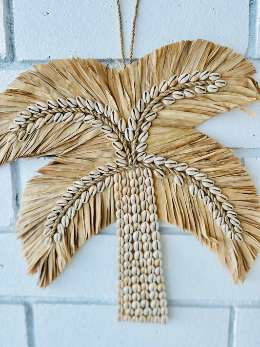 Decorative palm tree wall hanging with shell details on a white brick wall.