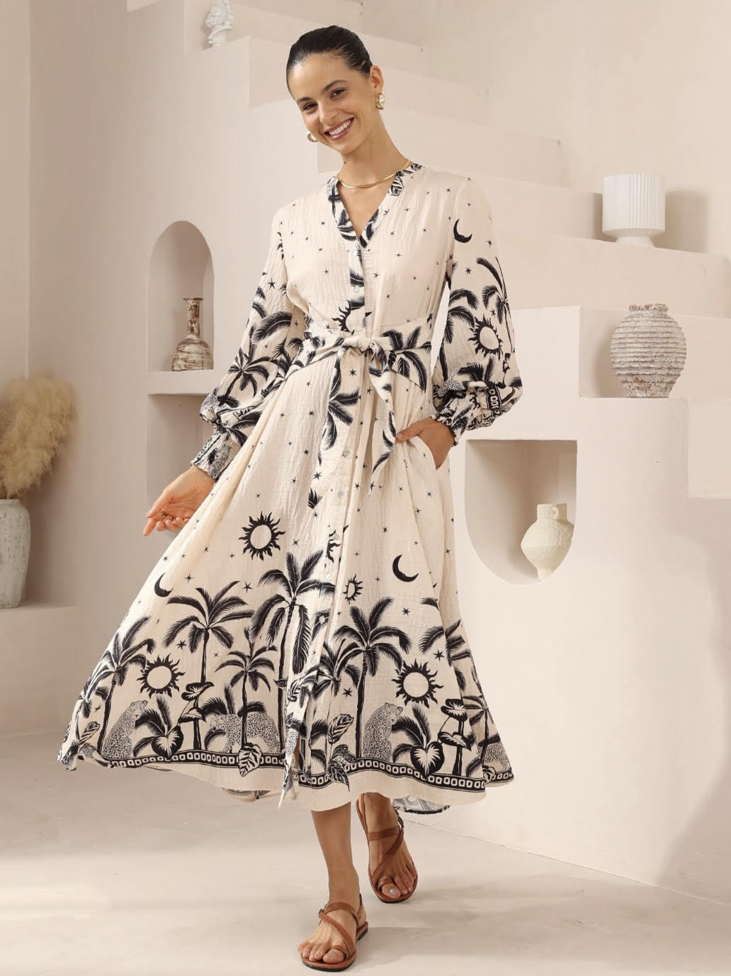 Woman wearing a white dress with black patterns in a minimalistic room.