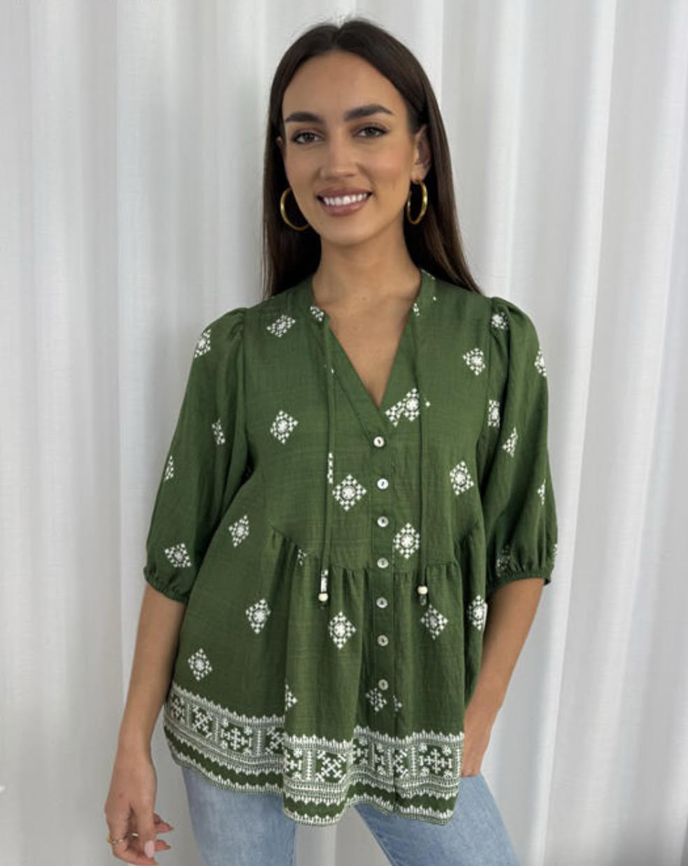 Woman wearing a green embroidered blouse against a white curtain background