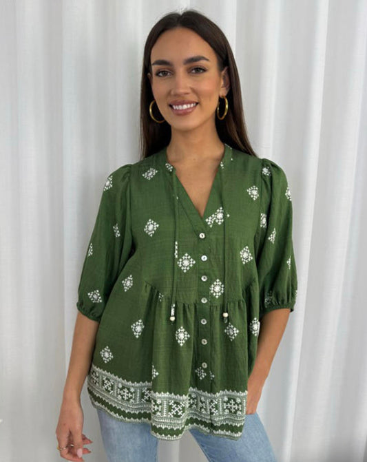 Woman wearing a green embroidered blouse against a white curtain background