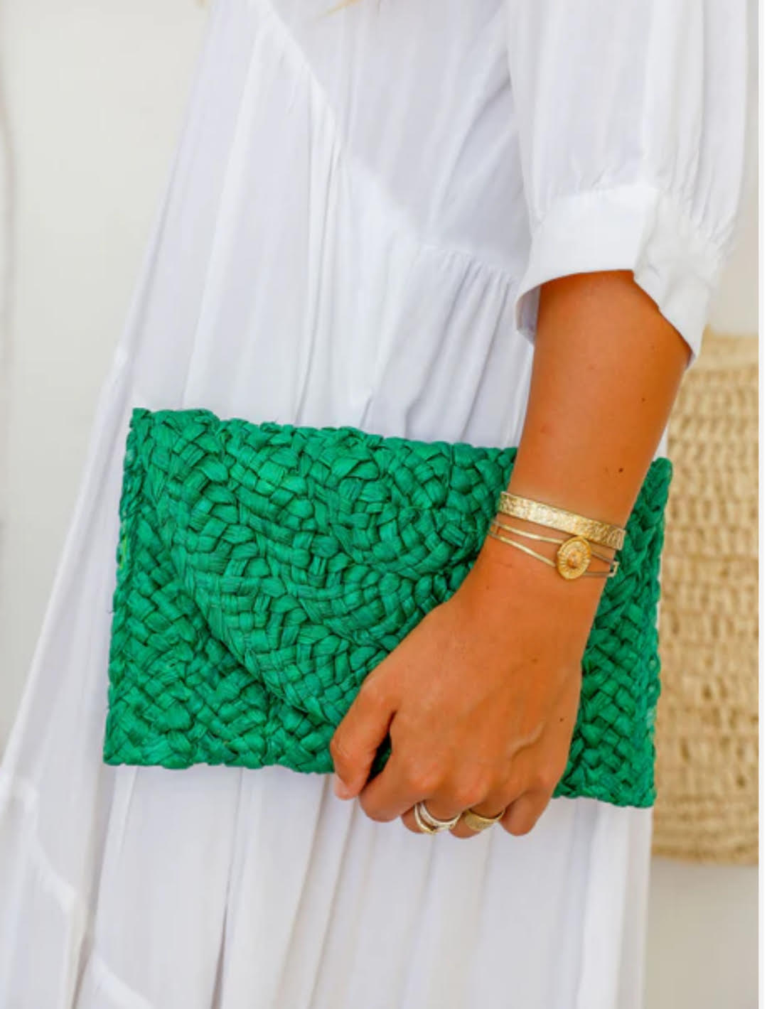 Person holding a green textured clutch bag with a white dress.
