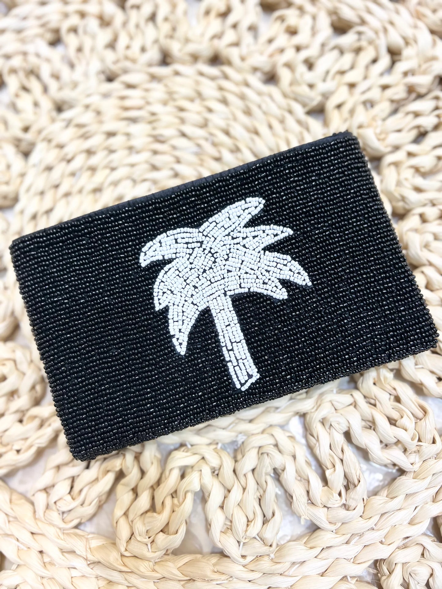 Black beaded pouch with a palm tree design on a woven surface