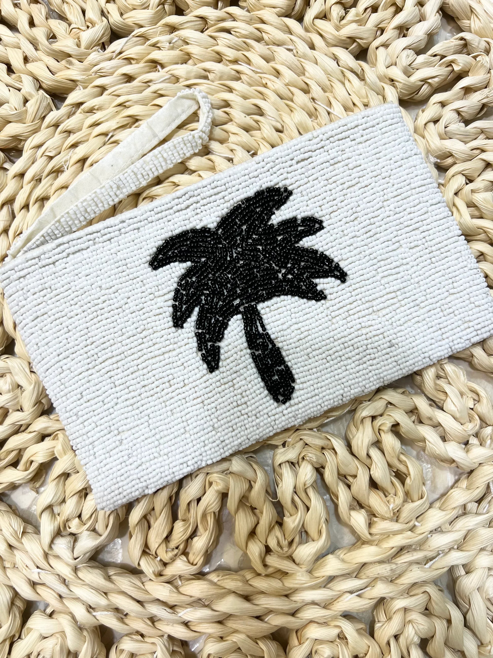 White pouch with black palm tree design on a woven surface
