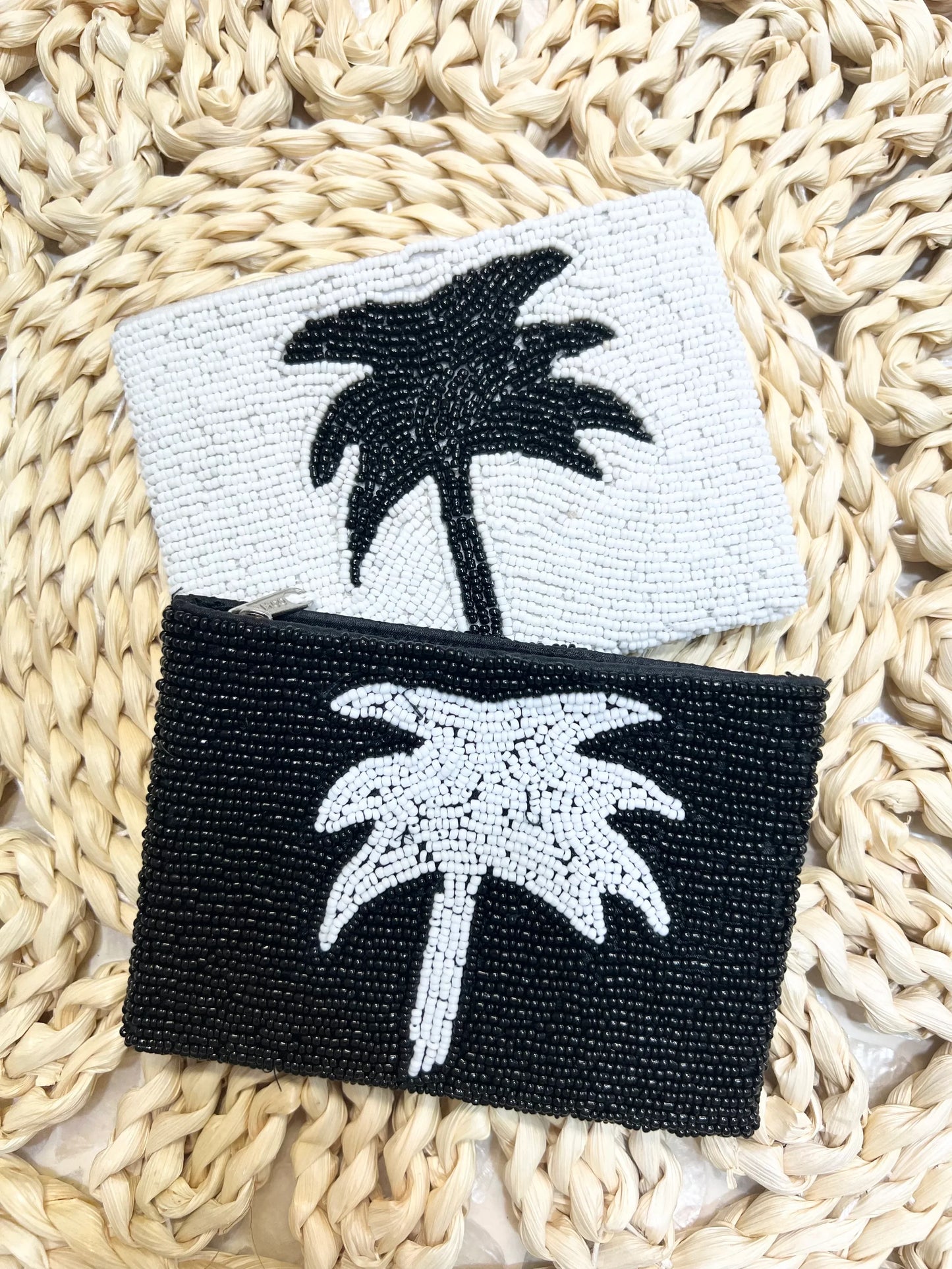 Two beaded palm tree coin purses, one black and white, one white and black, on a woven surface.