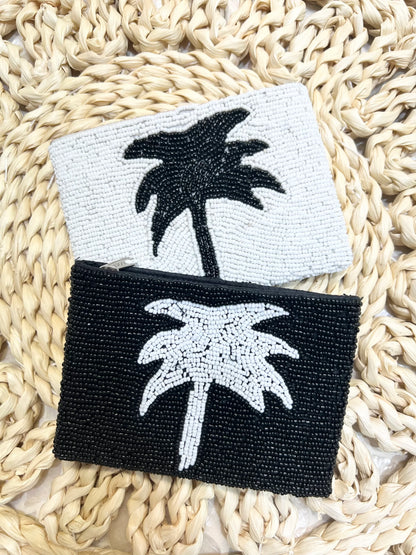 Two beaded palm tree coin purses, one black and white, one white and black, on a woven surface.