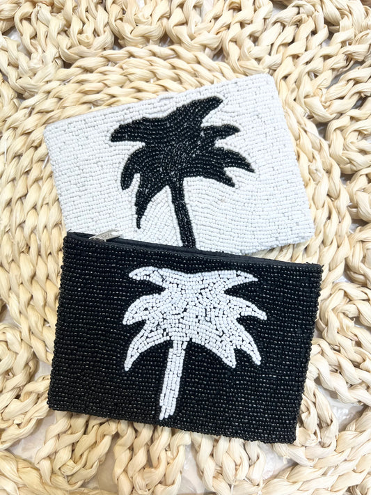 Two beaded palm tree coin purses, one black and white, one white and black, on a woven surface.