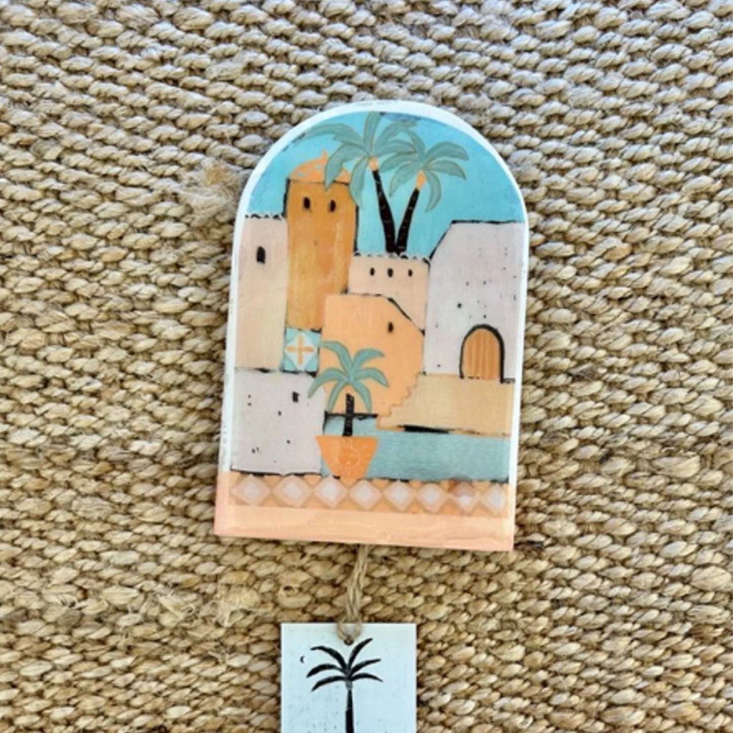 Decorative wall hanging with a colorful scene of buildings and palm trees on a textured surface.