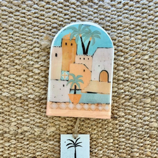Decorative wall hanging with a colorful scene of buildings and palm trees on a textured surface.