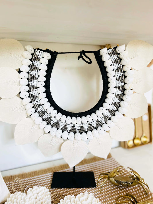 Black and white beaded shell necklace wall decor on a stand with a blurred background