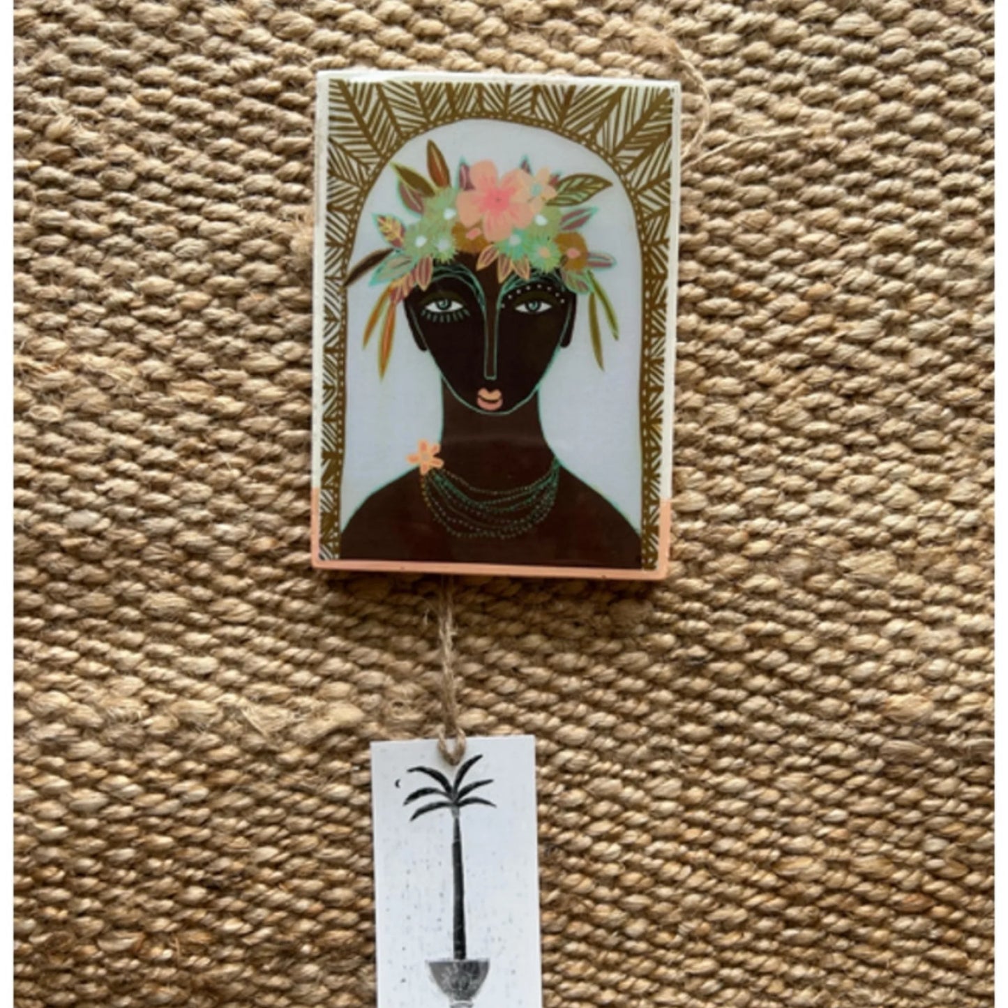 Decorative wall hanging with a stylized portrait of a woman with flowers in her hair on a textured surface.