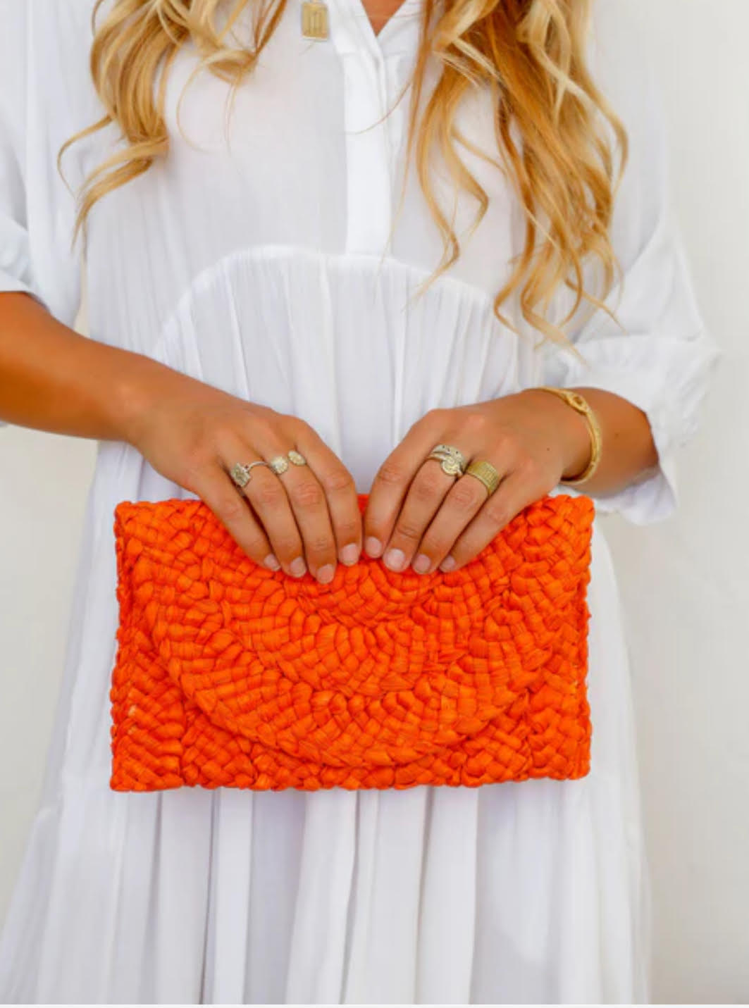 Person holding an orange clutch against a white background
