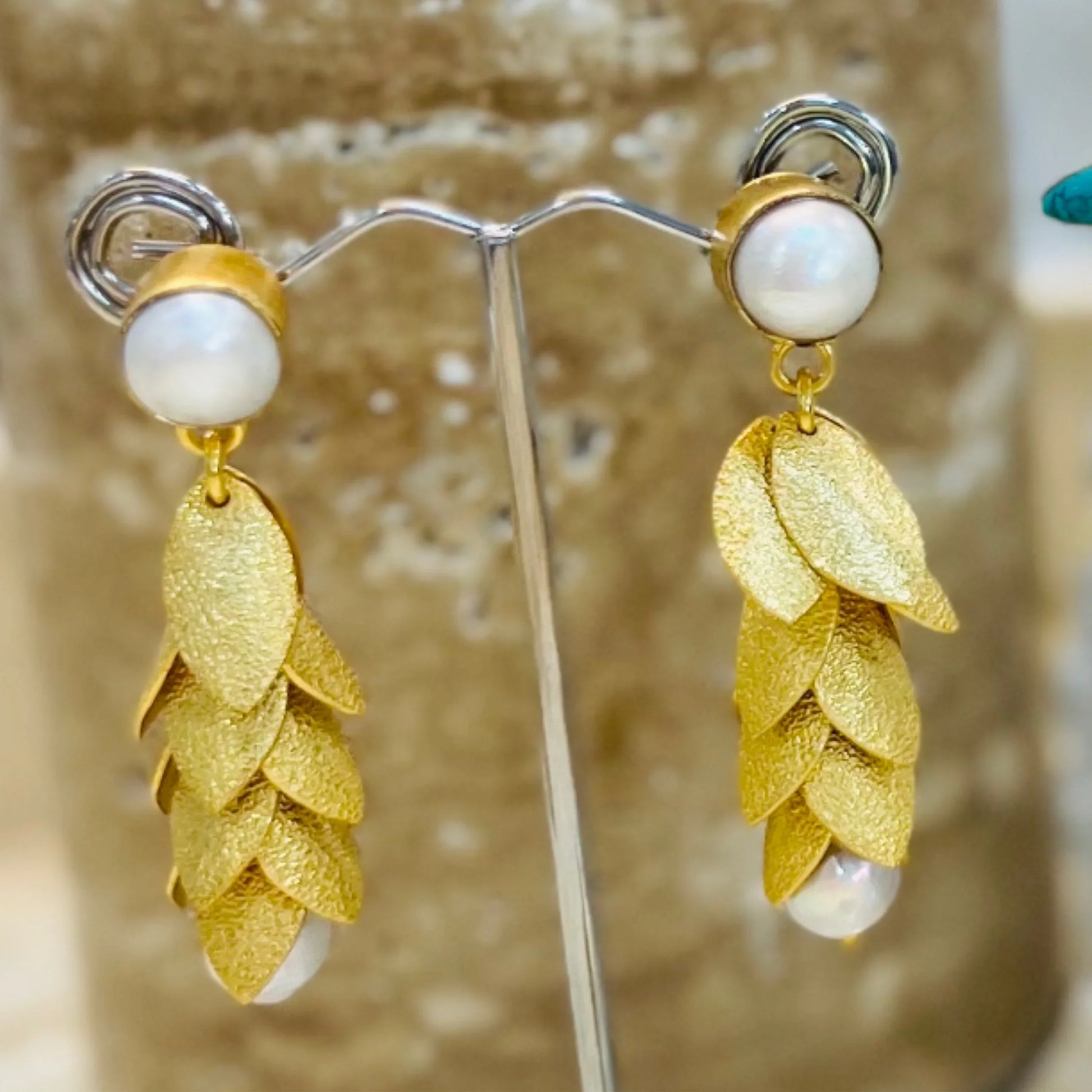 Gold leaf earrings with pearl accents on a stand against a neutral background