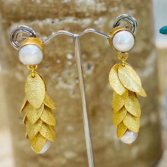 Gold leaf earrings with pearl accents on a stand against a neutral background