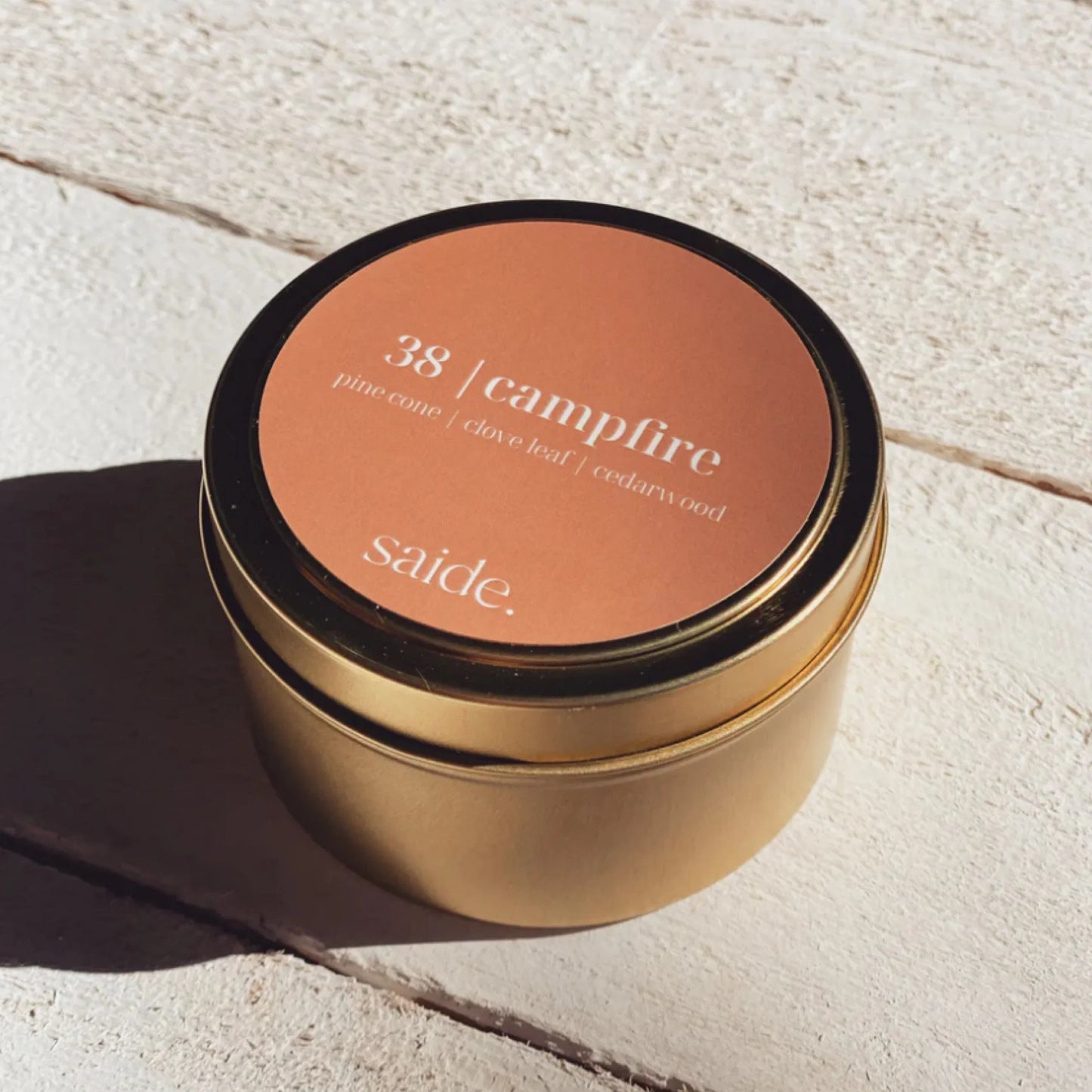 Gold candle jar with '38 campfire' label on a light stone surface