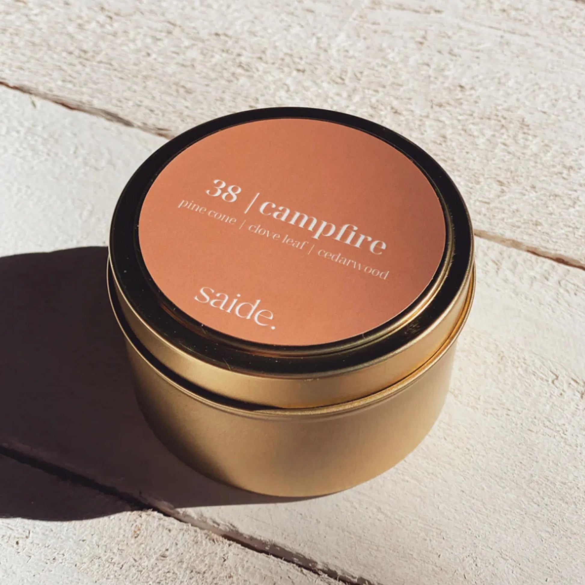 Gold candle jar with '38 campfire' label on a light stone surface