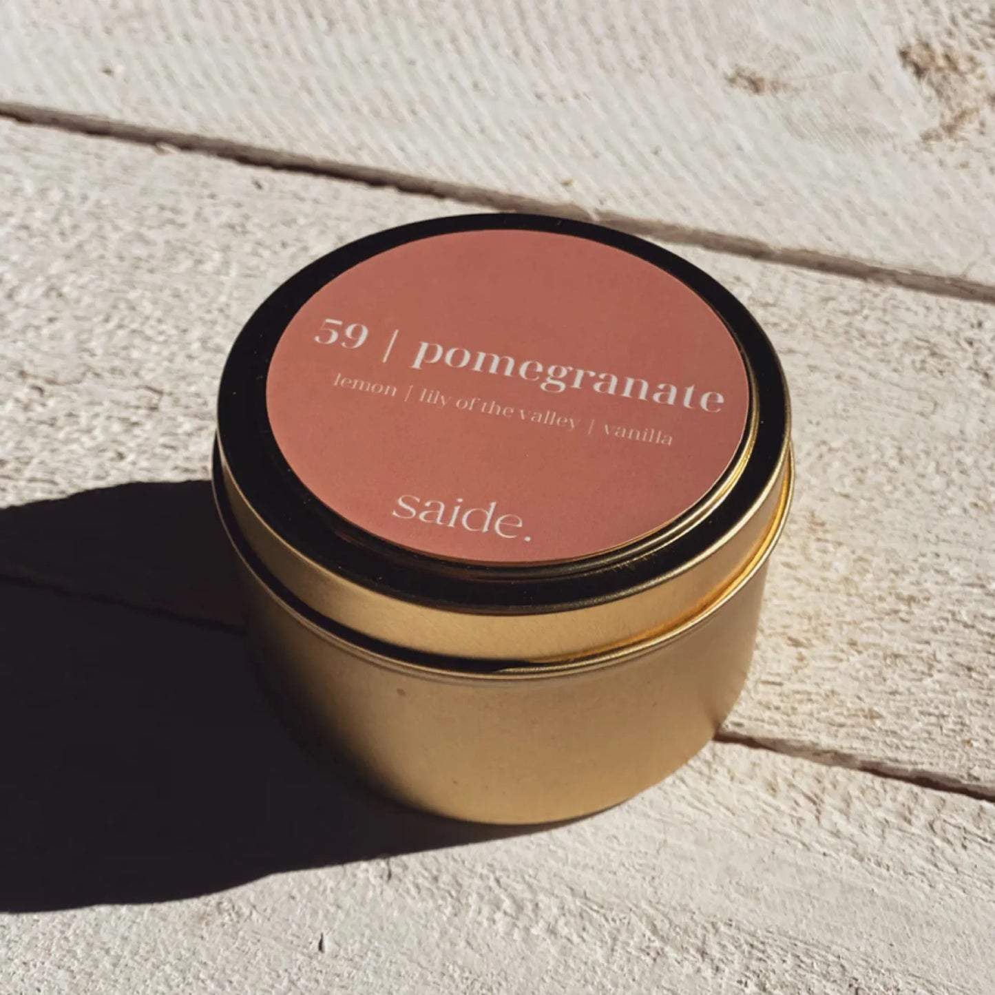 Gold candle jar with a pink lid on a light wooden surface