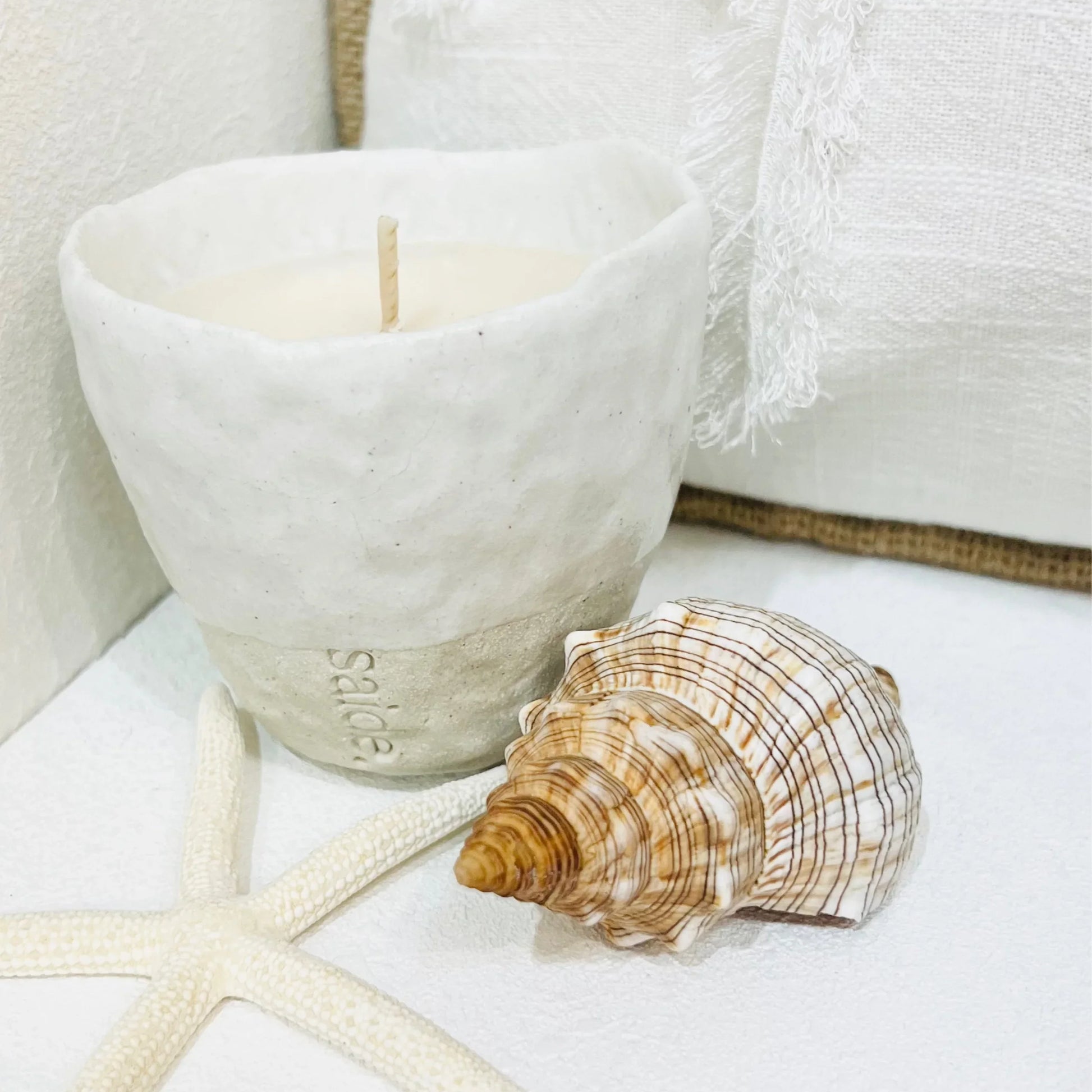 Candle in a white container with a shell and starfish on a white surface
